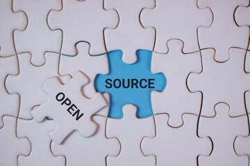A close-up of the puzzle pieces, highlighting the blue piece labeled SOURCE and the white piece labeled OPEN, symbolizing open source, collaboration, and sharing ideas within a team.