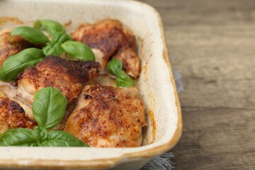 Tasty cooked chicken thighs with basil in baking dish on wooden table, closeup. Space for text