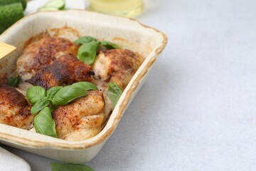 Tasty cooked chicken thighs with basil in baking dish on light grey table, closeup. Space for text