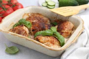 Tasty cooked chicken thighs with basil in baking dish and ingredients on light grey table, closeup