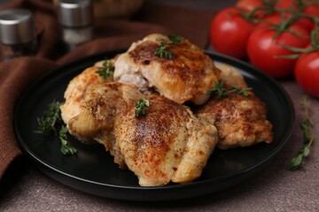 Tasty cooked chicken thighs with thyme and tomatoes on brown table, closeup