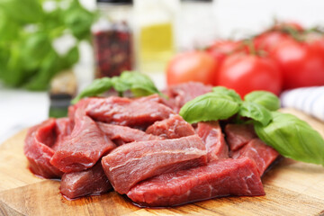 Pieces of raw beef meat, basil and ingredients on table, closeup