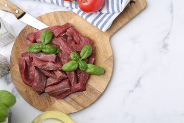 Pieces of raw beef meat, basil and ingredients on white marble table, flat lay. Space for text