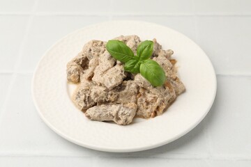 Tasty beef Stroganoff with basil on white tiled table, closeup