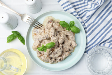 Tasty beef Stroganoff with basil on white tiled table, flat lay