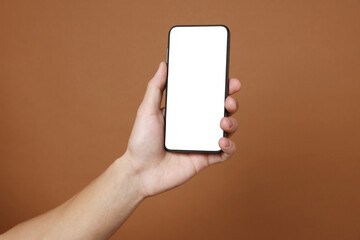 Man holding smartphone with blank screen on brown background, closeup. Mockup for design