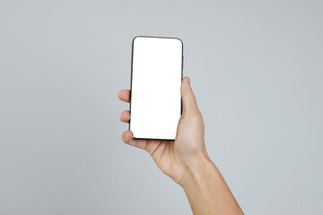 Man holding smartphone with blank screen on grey background, closeup