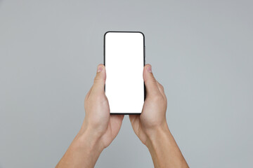 Man holding smartphone with blank screen on grey background, closeup