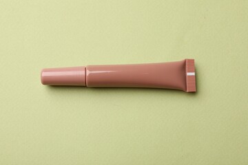 Beautiful nude lip gloss on light green background, top view