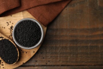 Aromatic black caraway in bowl and spoon on wooden table, top view. Space for text
