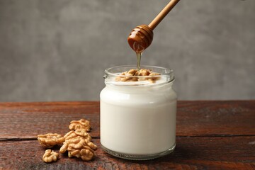 Dripping honey into Greek yogurt with walnuts at wooden table, closeup