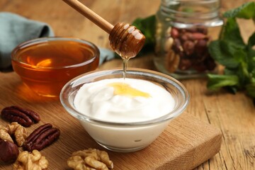 Dripping honey into Greek yogurt and nuts on wooden table, closeup