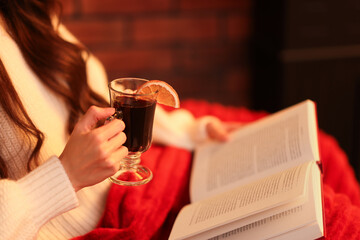 Woman with mulled wine reading book at home, closeup