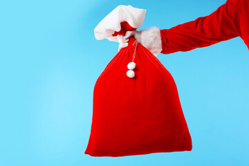 Santa Claus holding sack on light blue background, closeup. Merry Christmas and Happy New Year
