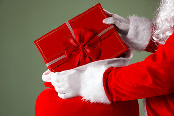 Santa Claus taking gift out of sack on grey background, closeup. Merry Christmas and Happy New Year