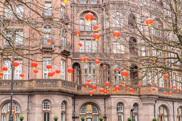 Manchester, uk, January 19th 2025 Vibrant red chinese new year  lanterns hang among bare tree branches above a grand brick building with arched windows