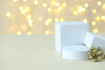 Empty podiums and Christmas decor on table against beige background with blurred lights, closeup with bokeh effect. Mockup for design