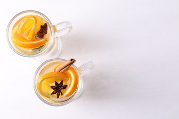 Tasty mulled wine with spices and orange slices in glass cups on white table, flat lay. Space for text