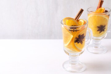 Tasty mulled wine with spices and orange slices in glass cups on white table, closeup. Space for text