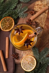 Tasty mulled wine with spices in glass cup, orange slices and fir branches on table, flat lay