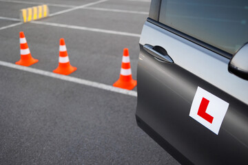 Learner driver vehicle approaching traffic cones during driving school training on an open asphalt area