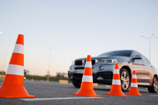 Row of bright orange traffic cones with an approaching SUV during driving practice on an open parking area