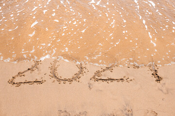 The number “202х” drawn on sandy beach as seawater washes over it, symbolizing closure, transition, and time moving forward.