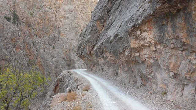 A narrow dirt road runs along the steep rocky cliffs of Kemaliye Canyon. The rugged landscape, vertical stone walls and dramatic terrain create a striking view of this remote mountain route.