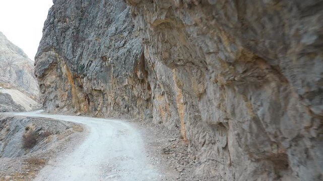 A narrow dirt road runs along the steep rocky cliffs of Kemaliye Canyon. The rugged landscape, vertical stone walls and dramatic terrain create a striking view of this remote mountain route.