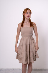 Confident red-haired woman posing in beige dress, studio portrait.
