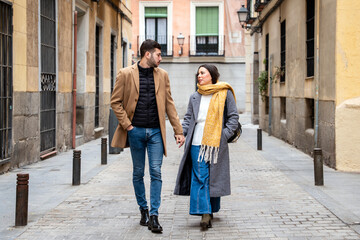 Couple strolls hand in hand through charming narrow streets of Madrid on a cool winter day