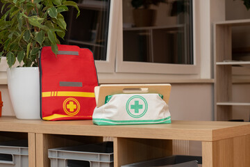 Red and green medical bags placed on wooden table in a bright room with plants, showcasing first aid supplies and organized healthcare essentials for emergency situations