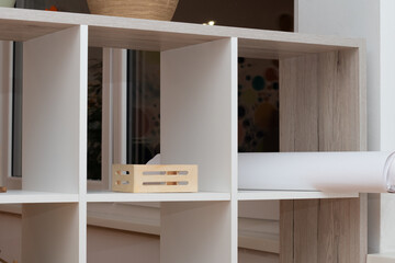 Modern wooden shelving unit with open compartments, featuring decorative items and a roll of paper, creating a stylish and organized interior space with copy space