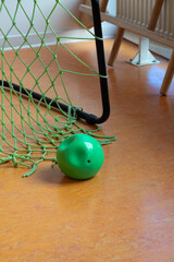 Green ball resting on orange floor near a sports net, showcasing playful indoor environment with vibrant colors and textures, ideal for children's activities and games