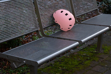 Pink bicycle helmet resting on a metal bench surrounded by greenery, showcasing safety gear in an outdoor setting with a tranquil atmosphere and natural elements