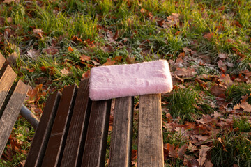 Soft pink fur blanket resting on a wooden bench surrounded by vibrant autumn leaves, creating a cozy and inviting outdoor atmosphere for relaxation and comfort