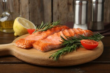 Pieces of tasty grilled salmon, rosemary and tomatoes on wooden table, closeup
