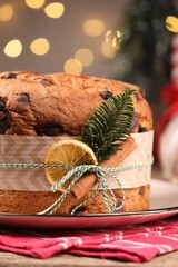 Tasty Christmas panettone cake with spices and fir branch on table against grey background with blurred lights, closeup. Bokeh effect