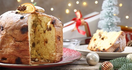 Tasty Christmas panettone cake with powdered sugar and festive decor on wooden table, closeup