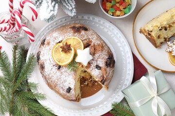 Tasty Christmas panettone cake with powdered sugar and festive decor on white table, flat lay