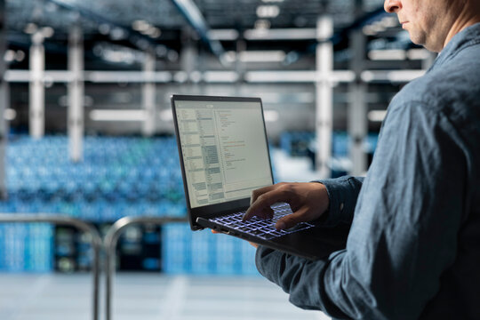 Close up of data center programmer coding on laptop, monitoring error logs for debugging processes. Server farm IT professional writing script, managing software updates for system stability