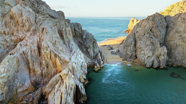 Aerial drone view revealing a secluded sandy cove nestled between towering cliffs near El Arco in Cabo San Lucas