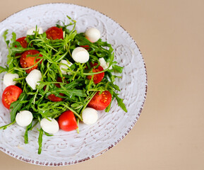 Fresh salad with cherry tomatoes, mozzarella cheese and arugula. Blue background. Close up. Copy space. plate of pesto pasta salad, tomatoes, green basil and mozzarella on wooden table