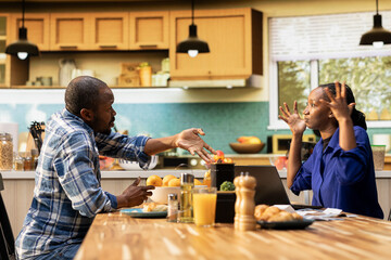 Angry boyfriend and girlfriend having an argument about finances. Woman holding receipts and the man gestures in frustration, yelling and blaming each other, irresponsible money management.