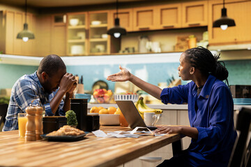 Man and woman fighting over unpaid bills and taxes at the kitchen table. Couple looks angry and worried, blaming each other for money issues and the stress of financial responsibility.