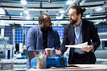 Multiethnic team of engineering specialists working together for solar power manufacturing process,...