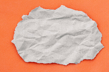 A wrinkled gray piece of torn paper sits on an orange textured backdrop, emphasizing contrast and...