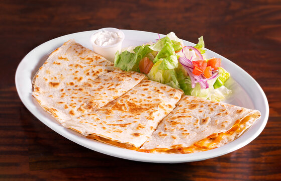 Chicken quesadilla platter with garden salad and sour cream in a white plate on a wooden table; copy space