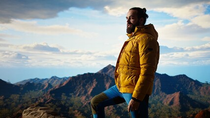 Proud explorer basks in the joy of accomplishment standing at the mountain peak with arms lifted,...