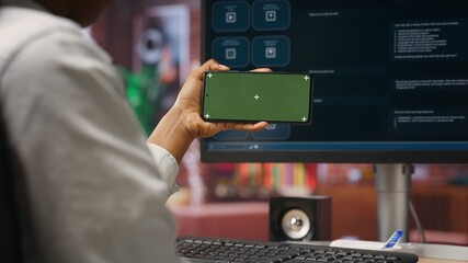 Woman using green screen smartphone to learn how to use AI LLM chatbot on computer screen in home...